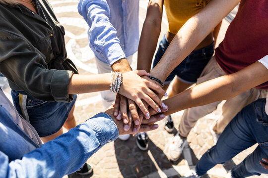 High angle view of multiracial friends stacking hands - Group of young college students work team celebrating together outdoors - Community, teamwork, unity and friendship concept