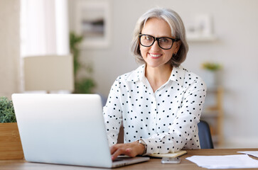 Beautiful senior business woman wearing glasses enjoying remote job on laptop