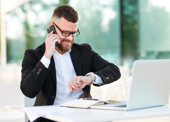 Smiling businessman making call by mobile phone and waiting for business partner at outdoor cafe