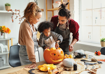 Happy african american family mother, father and child son carving pumpkin for Halloween holiday...