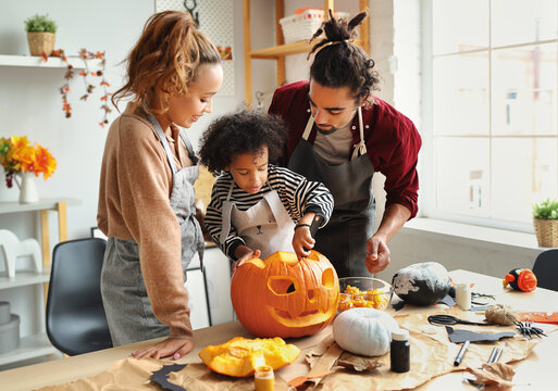 Happy African American Family Mother, Father And Child Son Carving Pumpkin For Halloween Holiday Together At Home