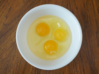 Three eggs in a white bowl on wood table