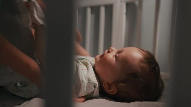 Adorable newborn baby boy, don't want to sleep in crib at night. Mother puts baby to bed.
