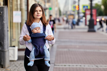 Woman walks with baby in sling on crowded street.
