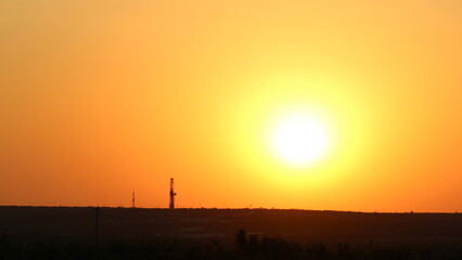 Fototapeta na wymiar Two drilling rigs peak over the horizon with a firing red sunset view across the skyline in West Texas Permian Basin