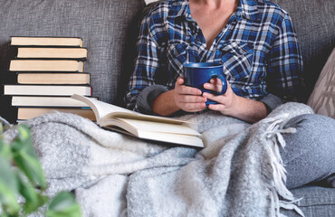 Woman sitting on couch reading book and drinking coffee or tea