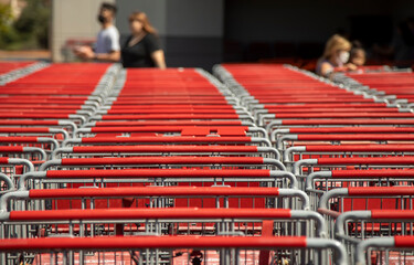 A row of red shopping carts with people wearing masks diffused in the background