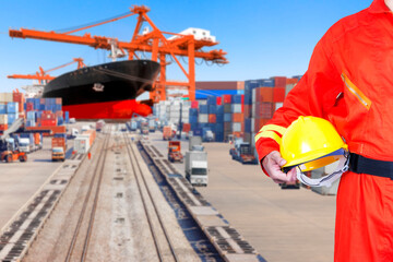 Dock worker holding hard hat for controlling work process container ship being unloaded with  in the harbor