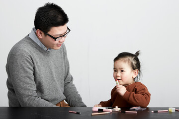 Fototapeta na wymiar Asian little girl and parents playing makeup game, indoor white background