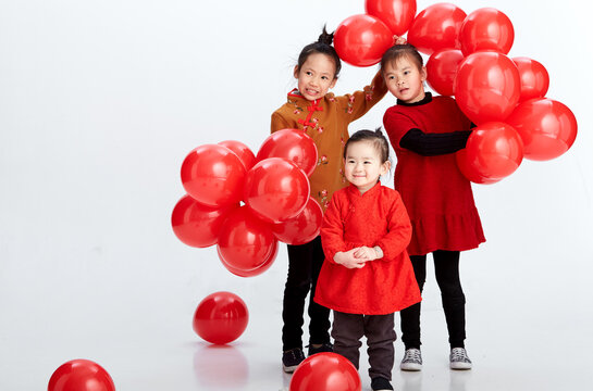 Cute Asian little sisters are playing with red festive balloons indoors with white background