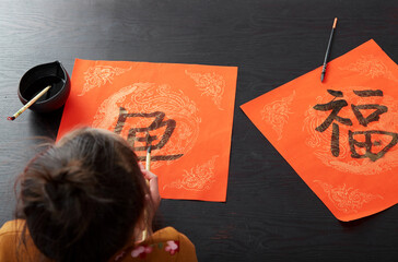 Cute Asian little girls are writing a copybook with traditional Chinese New Year atmosphere, indoors