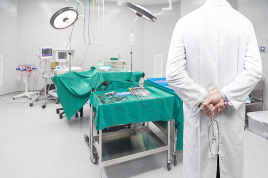 rear view image of doctors pose arms crossed behind back with stethoscope looking at operating room of a modern hospital