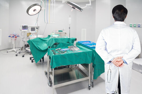 rear view image of doctors with stethoscope pose arms crossed behind back looking at operating room in a modern hospital