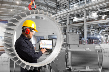 Engineer using computer for maintenance seen through frame of large motor equipment at factory...