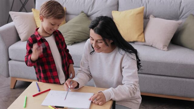 Parent mother teaching child boy drawing using colorful pencils in paper. Caucasian mother with her son chatting enjoy common hobby and leisure activity. Family enjoying spending free time together.