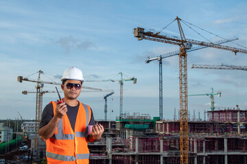 Foreman holding blueprint for control working by radio communication at high building construction site
