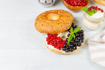 Bagel with cream cheese and fresh berries. On a light wooden background, horizontal, with space. Close-up