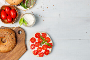 Open bagel sandwiches with cream cheese, sweet tomatoes and mixed salad. Top view, on a light wooden background. A copy of the space.