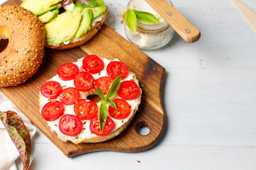 Open bagel sandwich with cream cheese, sweet tomatoes and avocado. Close-up on a light gray background