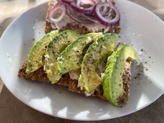 Bright green avocado slices on cracker bread with red onion in background. 