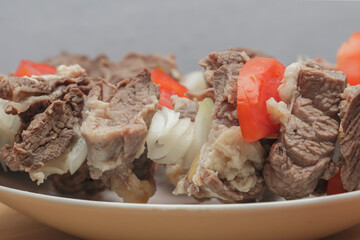  raw goat meat with chopped tomatoes and onions on skewers on a wooden board close up side view
