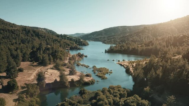 Sunset mountain river. Aerial forest wild nature landscape. Dam barrage, blue river, green forest scene. Sunlight over turquoise water reservoir in countryside landscape. Hydropower, green energy.