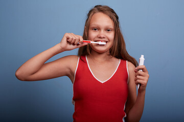 a beautiful girl of 11 years old brushes her teeth on a blue background