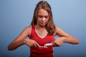 a beautiful girl of 11 years old brushes her teeth on a blue background