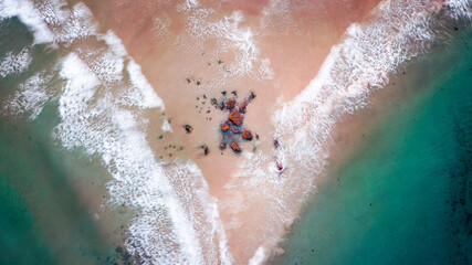 Overhead shot of waves crashing over a sand bar with rocks in a v shaped pattern, green water either side