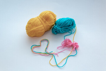Green, yellow and pink wool threads. The outline of a heart made of woolen threads. Balls of coiled woolen threads.
