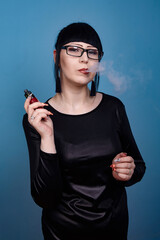 A beautiful girl with dark hair and glasses exquisitely smokes an electronic cigarette