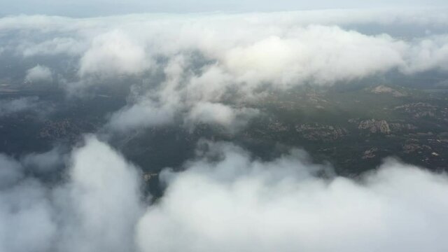 View from above, drone point of view, stunning aerial video of a drone flying over some fluffy moving clouds with a valley in the distance.