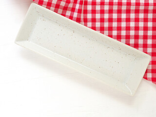 Top view, Empty long rectangle white plate with brown dot on red and white checkered fabric napkin...