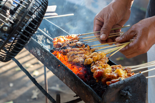 Chicken satay on traditional charcoal fire. satay on fire with smoke and an appetizing look. hands cooking satay on the grill
