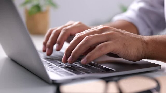 Close-up of man hands typing on laptop keyboard on white table at home office or workplace. 