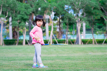 Child playing sports are wondering and looking at something. Cute girl holds a badminton racket and a badminton ball in her hand.