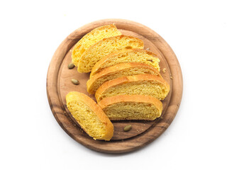 Slice of yellow pumpkin bread roll on round wooden board on white background