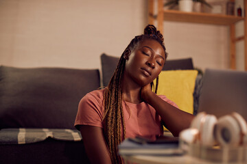 Fototapeta premium Young African American woman feels exhausted after e-learning over laptop in the evening at home.