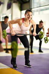 Happy athletic woman lifts barbell during strength training in gym.