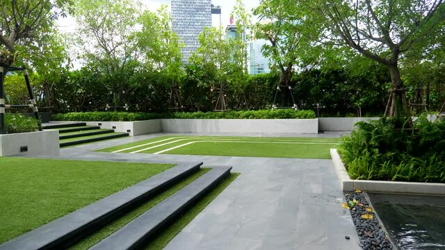 First Person View Walk On Green Trees Garden for Residents on Rooftop of Residential Apartments Building. Common Relaxing Area in Condominium. Resting Place on Roof of Skyscraper in Capital City.