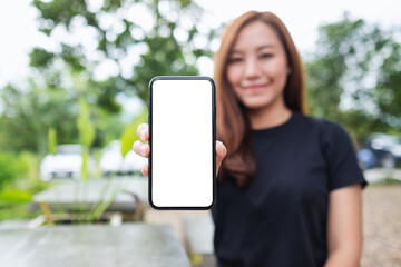Mockup image of a woman holding and showing a mobile phone with blank white screen in the outdoors