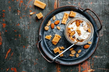 Delicious ice cream served with caramel and hazelnuts in a glass jar on a blue tray, banner, menu, recipe place for text, top view