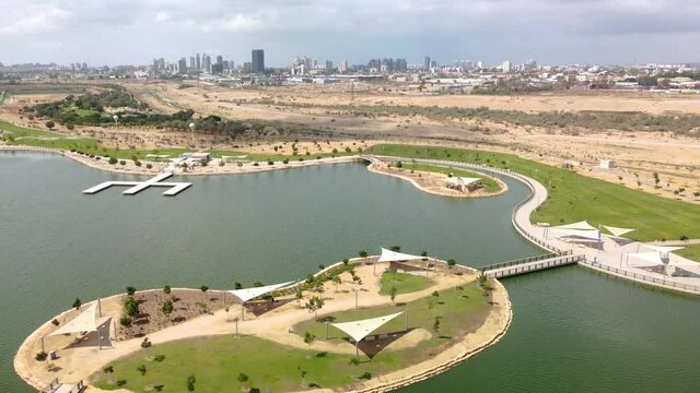Flying from right to left over the artificial lake in the park with Beer Sheva buildings at background
