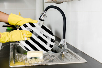 Human hand in yellow rubber gloves washing dishes in the kitchen sink.