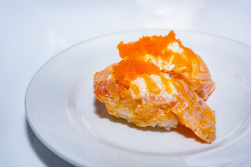 Close-up, Salmon fillets burn with salad cream sauce sprinkled with ebiko on a white plate on a white table.