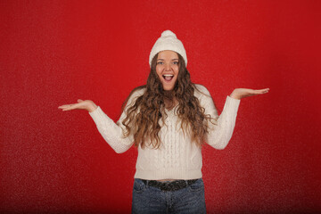a happy girl in a winter hat and a knitted sweater in jeans on the background of artificial snow