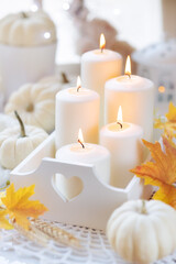 Hello Autumn or Happy Thanksgiving concept with a beautiful cozy composition of burning candles and decorative white pumpkins and autumnal leaves. Shallow depth of field