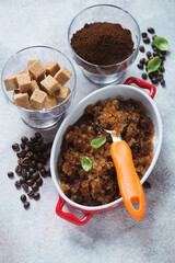Glass container with coffee granita and a serving spoon, vertical shot on a beige stone surface, elevated view