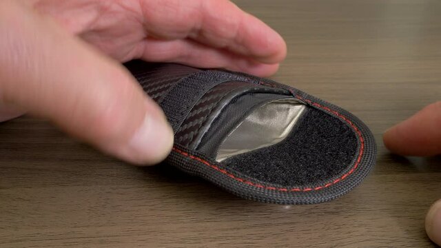 Closeup POV shot of a man&rsquo;s hands sliding a keyless fob into a radio signal-blocking / Faraday pouch, to prevent unauthorized access to a vehicle.