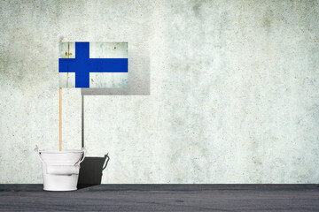 Flag of Finland on a stick, in a small bucket, against the background of a concrete wall. Copy space. Signs and Symbols.